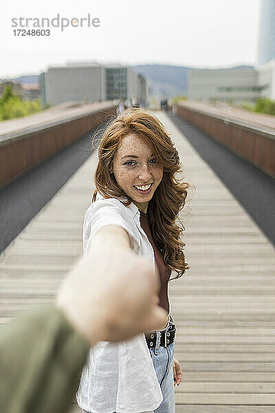 Freundin lächelt  während sie die Hand ihres Freundes auf einer Brücke hält