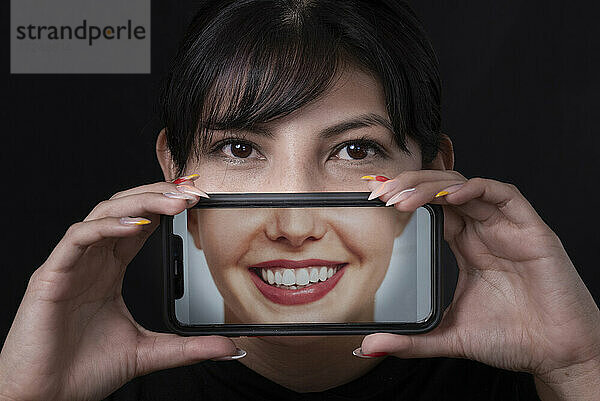 Lächelnde schöne Frau nimmt Selfie durch Smartphone auf schwarzem Hintergrund
