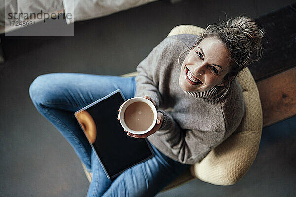 Glückliche Besitzerin hält eine Cappuccino-Schale  während sie in einem Café sitzt
