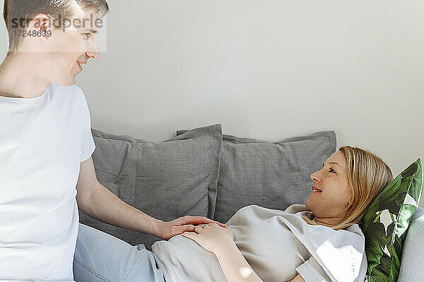 Fürsorglicher Ehemann betrachtet seine schwangere Frau auf dem Sofa im Wohnzimmer liegend