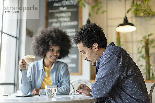 Männlicher Kunde liest Vertrag  während er mit einer Unternehmerin in einem Café sitzt
