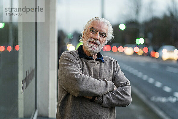 Älterer Mann mit verschränkten Armen vor einem Cafe stehend