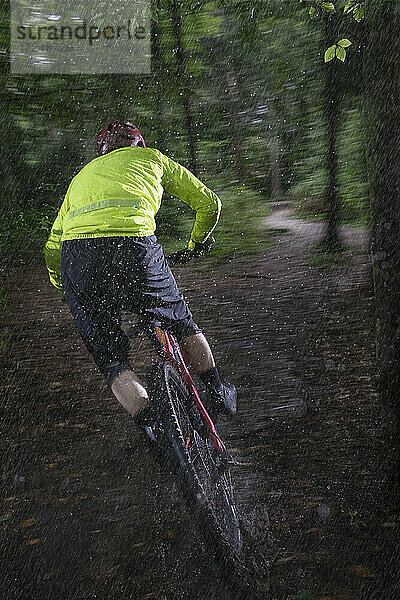 Mann fährt Fahrrad auf unbefestigtem Weg im Wald bei Regen