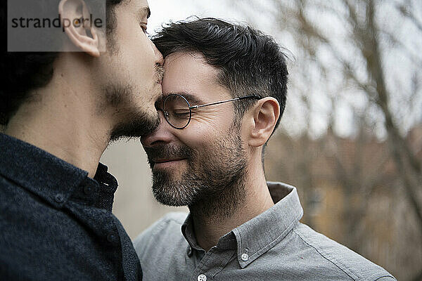 Mittlerer erwachsener Mann küsst im Freien auf die Stirn eines männlichen Freundes