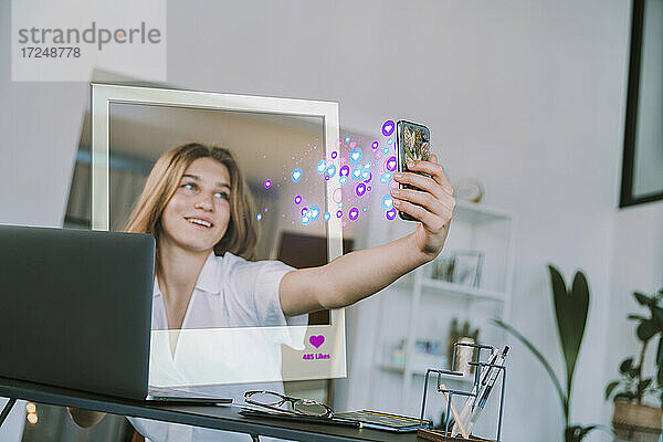 Weibliche Teenager-Influencerin  die mit ihrem Handy ein Selfie mit einem Symbol für soziale Medien zu Hause macht