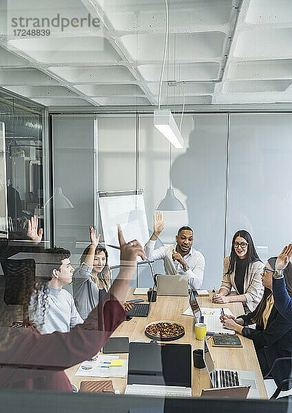 Multiethnische Gruppe von männlichen und weiblichen Fachkräften mit erhobenen Händen während einer Sitzung im Büro