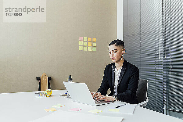 Geschäftsfrau mit In-Ear-Kopfhörern und Laptop im Büro