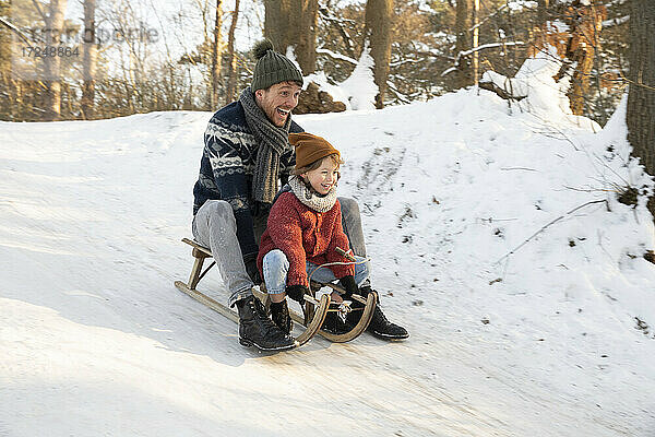Verspielter Vater und Sohn beim Schlittenfahren auf Schnee im Winter