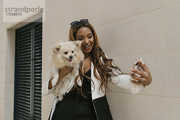 Schöne Frau hält Hund und nehmen selfie durch Handy von der Wand