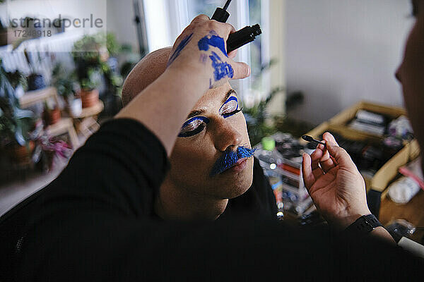 Eine Maskenbildnerin schminkt ein männliches Modell im Studio