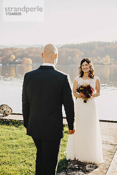 Glückliche Braut schaut Bräutigam an  während sie am See steht