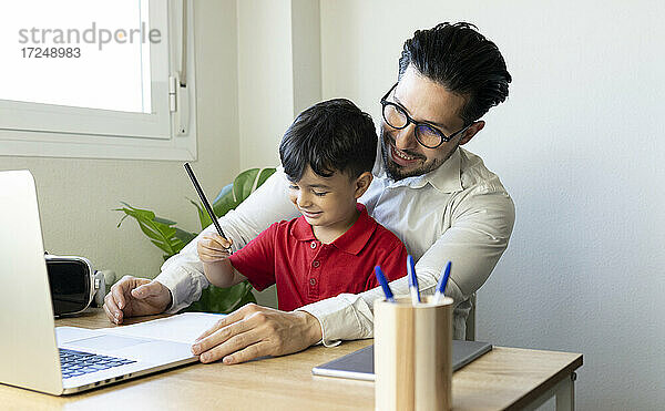 Geschäftsmann schaut auf einen Laptop  während er mit seinem Sohn zu Hause sitzt