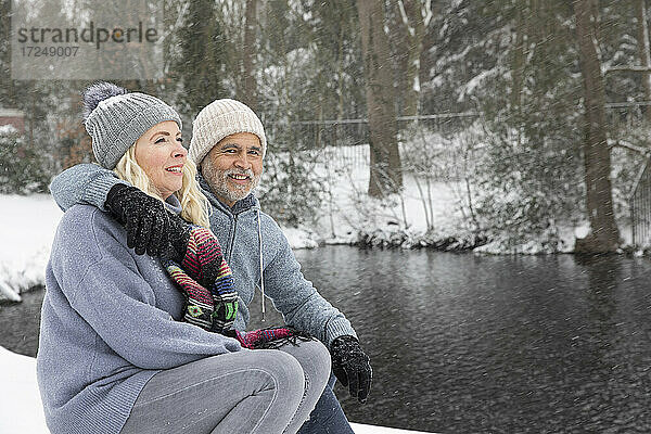 Mann  der eine Frau umarmt  während er im Winter am See sitzt