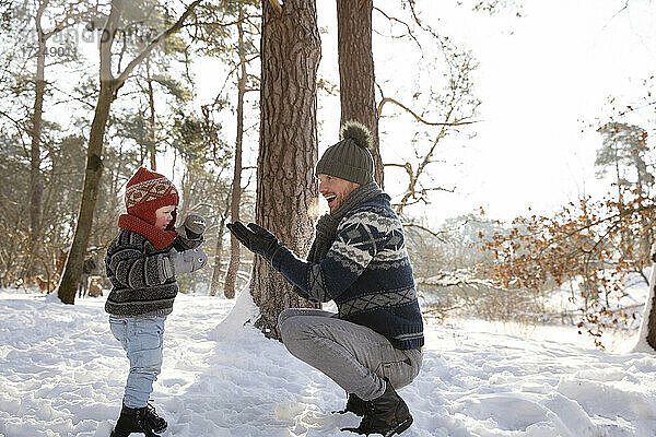 Vater spielt mit seinem Sohn  während er im Winter im Schnee hockt