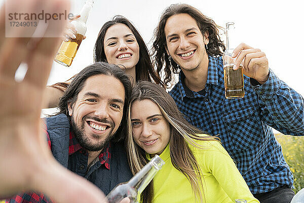 Glückliche Freunde zeigen Bierflaschen vor dem Himmel