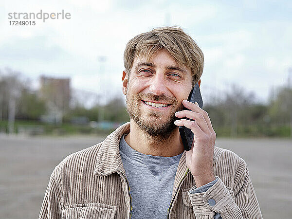 Lächelnder gutaussehender Mann  der mit einem Mobiltelefon spricht