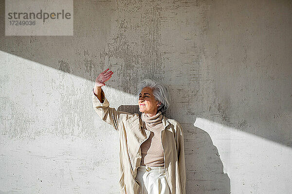 Frau schaut weg  während sie an einem sonnigen Tag vor einer Mauer steht