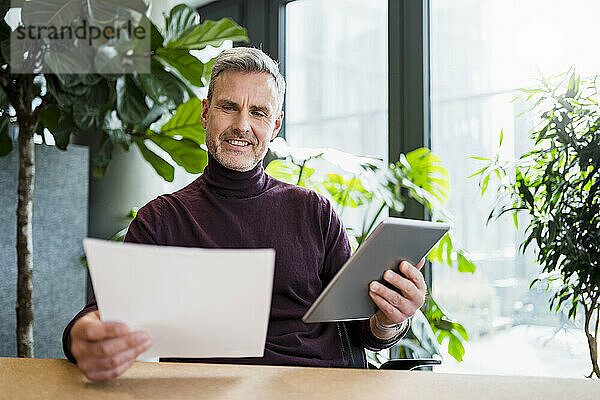 Älterer Geschäftsmann mit digitalem Tablet und Dokument im Büro