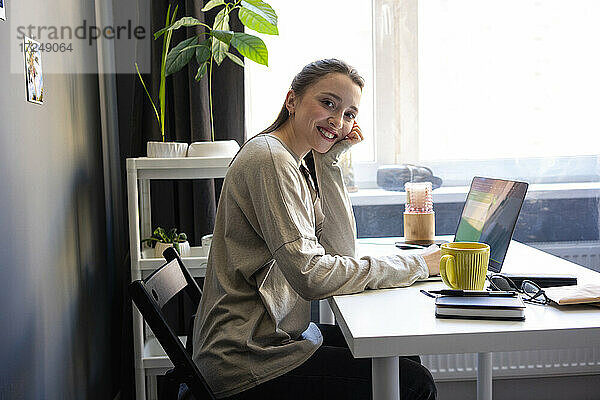Lächelnde Frau sitzt am Laptop im Home Office