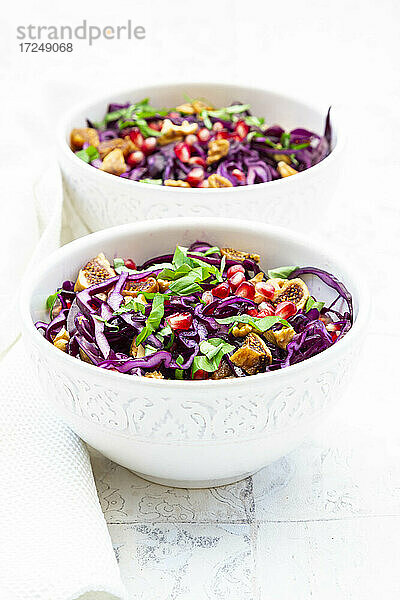 Zwei Schalen veganer Salat mit Rotkohl  Granatapfelkernen  getrockneten Feigen  Walnüssen und Basilikum