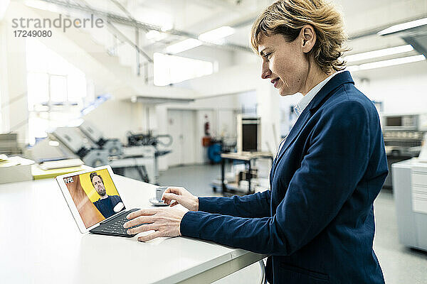Ältere Geschäftsfrau  die einen Kollegen bei einem Videogespräch über ein digitales Tablet in einer Werkstatt beobachtet