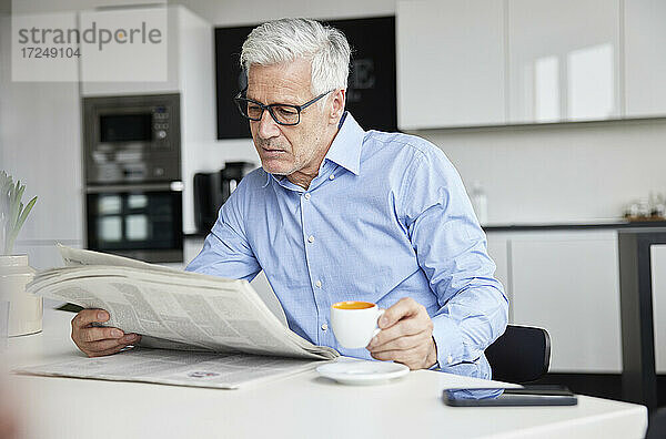 Älterer Geschäftsmann mit Kaffeetasse  der in einer Cafeteria Zeitung liest