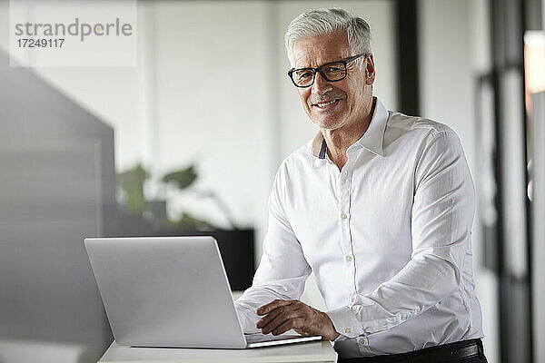Lächelnder männlicher Unternehmer mit Laptop im Büro