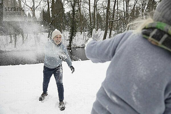 Verspielter Mann  der im Winter Schnee auf eine Frau wirft
