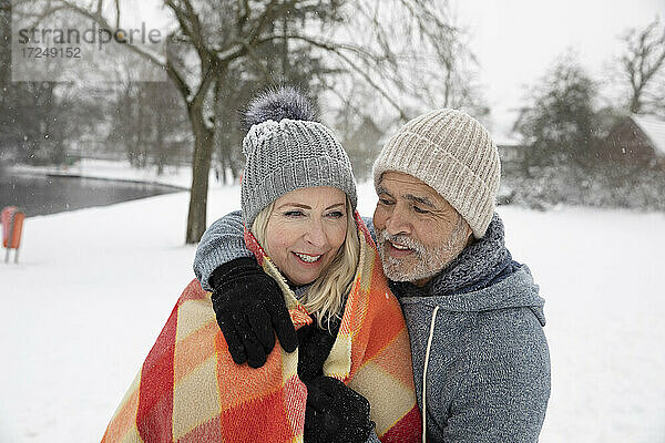 Mann umarmt Frau in Decke im Winter