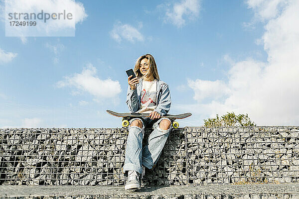 Lächelnde Frau mit Mobiltelefon an einer Felswand sitzend