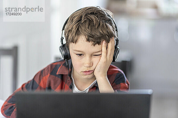 Junge langweilt sich während des Online-Unterrichts  der zu Hause stattfindet
