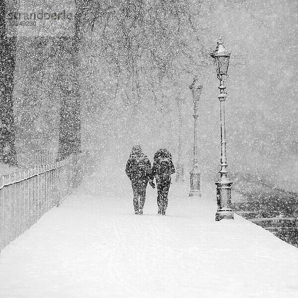 Paar  das bei starkem Schneefall gemeinsam in einem verschneiten Park spazieren geht