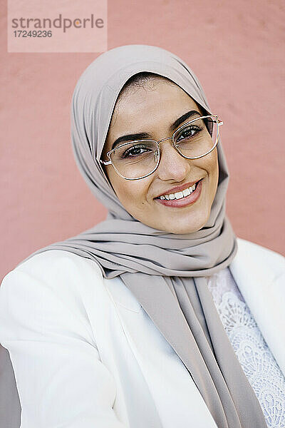 Lächelnde Frau mit Brille vor einer rosa Wand