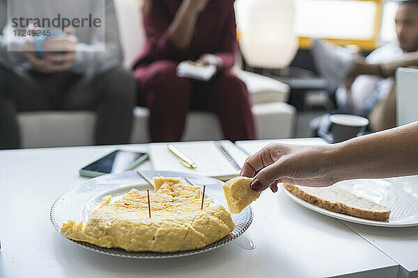 Geschäftsfrau isst spanisches Omelett am Tisch mit Kollegen im Hintergrund