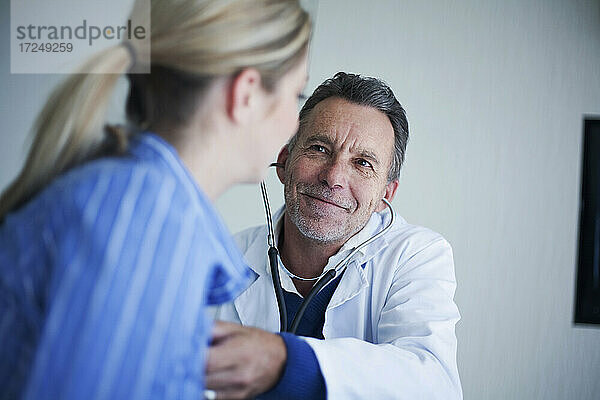 Lächelnder männlicher Oberarzt  der eine Patientin mit Stethoskop im Krankenhaus untersucht