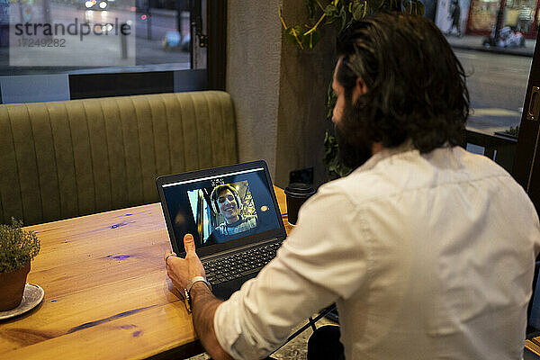Junger Mann unterhält sich mit einem Freund über einen Videoanruf am Laptop im Restaurant