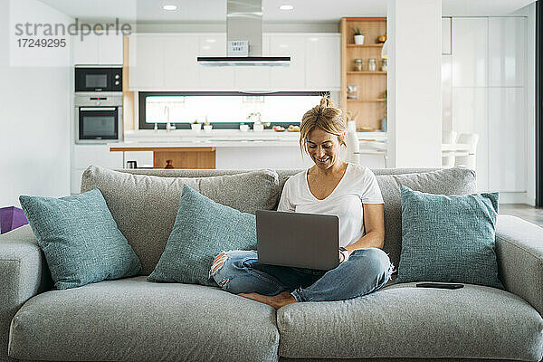 Berufstätige Frau  die zu Hause auf dem Sofa sitzend einen Laptop benutzt
