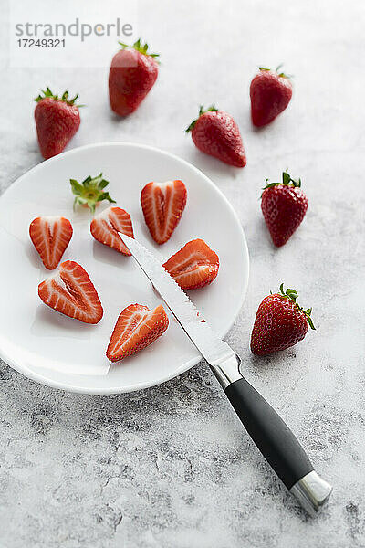 Küchenmesser und Teller mit frischen Erdbeeren auf weißem Marmor liegend