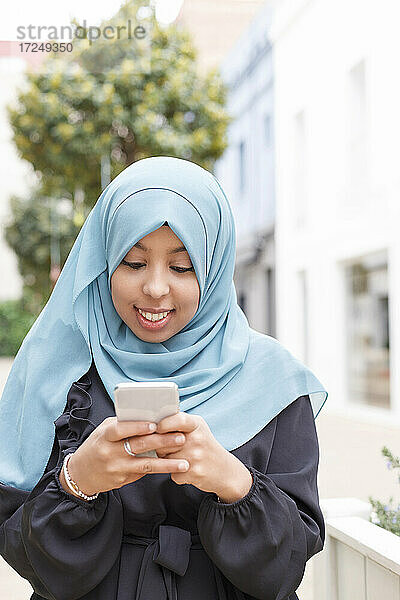 Junge Frau mit blauem Hidschab und Smartphone