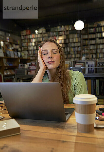 Junge Frau mit geschlossenen Augen sitzt in einer Bibliothek
