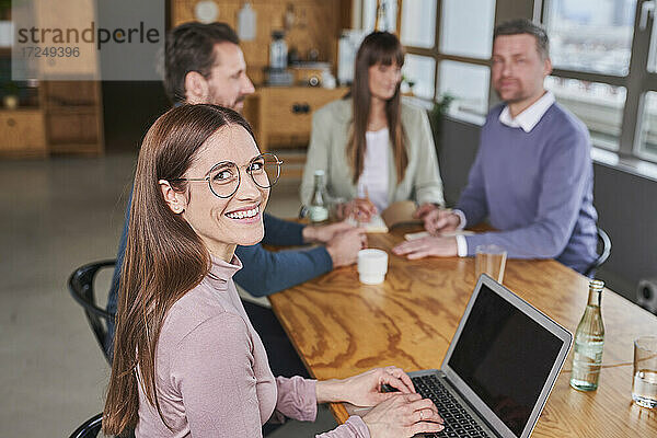 Lächelnde Unternehmerin mit Kollegen im Hintergrund im Sitzungssaal
