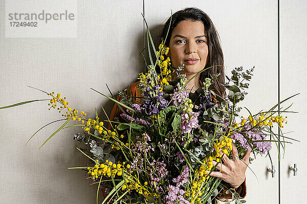 Mittlere erwachsene Frau hält einen Blumenstrauß  während sie vor einer Wand steht