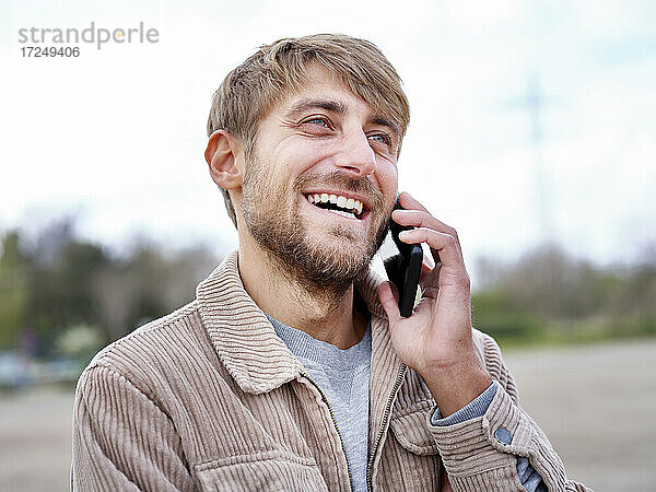 Glücklicher bärtiger Mann  der wegschaut  während er mit seinem Smartphone telefoniert