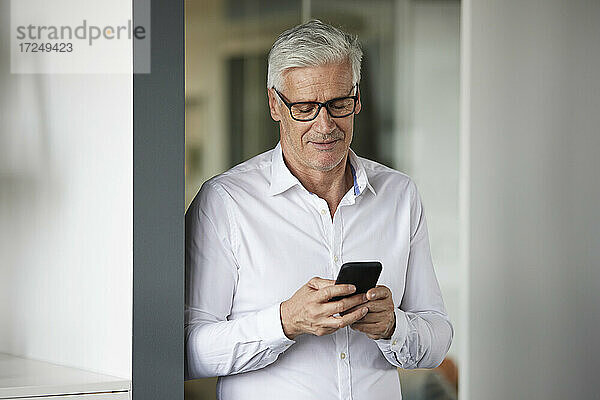 Geschäftsmann  der ein Mobiltelefon benutzt  während er im Büro steht