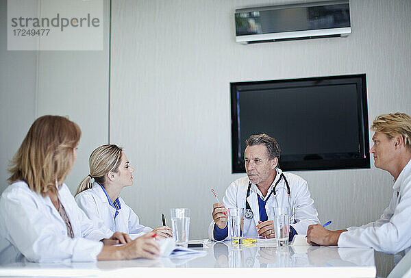 Oberarzt im Gespräch mit männlichen und weiblichen Mitarbeitern des Gesundheitswesens während einer Besprechung im Krankenhaus
