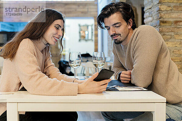 Junges Paar  das in einem Restaurant sitzt und auf sein Smartphone schaut