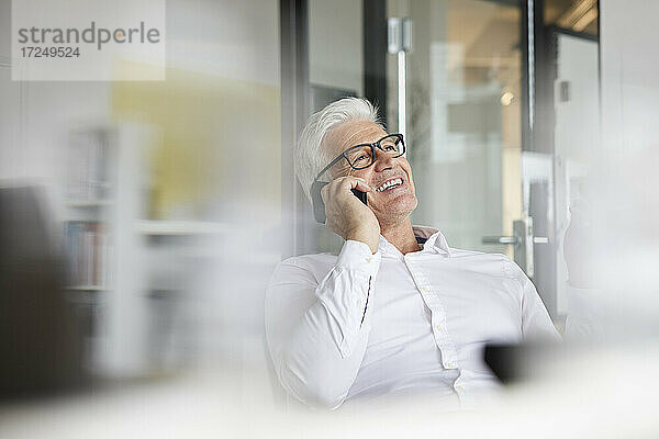 Männlicher Unternehmer  der lächelt  während er im Büro mit einem Mobiltelefon spricht