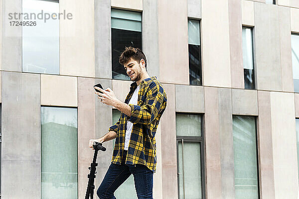 Lächelnder Mann  der ein Mobiltelefon benutzt  während er vor einem Gebäude steht