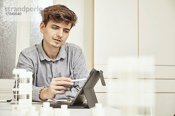 Junger männlicher Architekt bei der Arbeit über einem digitalen Tablet am Tisch
