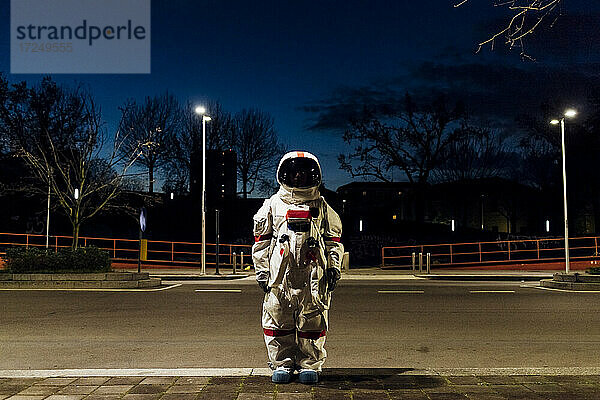 Junge Astronautin im Raumanzug auf nächtlichem Fußweg stehend